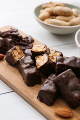 Board with tasty chocolate candies on light wooden background, closeup