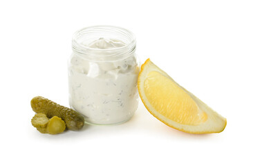 Glass jar with tasty tartare sauce, lemon and pickled cucumbers on white background