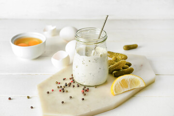 Glass jar with tasty tartare sauce and ingredients on light wooden background
