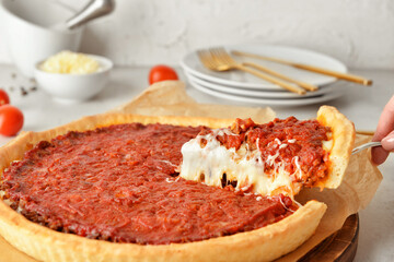 Woman taking piece of tasty Chicago-style pizza on light background