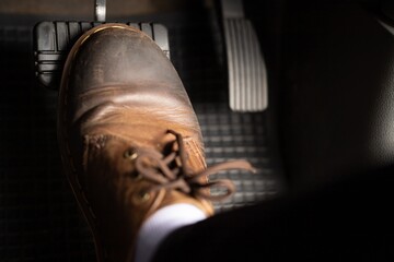 A man in brown leather shoes is stepping on the brakes of a car.