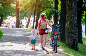 A woman with her daughter and a bicycle walks in the park