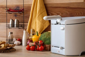 Modern deep fryer and products on table near wooden wall