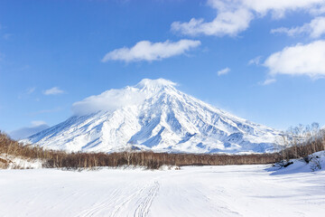 Fototapeta na wymiar Russia, Kamchatka Volcanoes Natural Park. A snow-covered road along a frozen riverbed in the direction of an icy volcano. Winter hiking to the Avachinsky pass.
