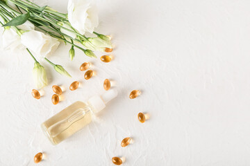 Fototapeta na wymiar Cosmetic dropper bottle, pills and flowers on light background