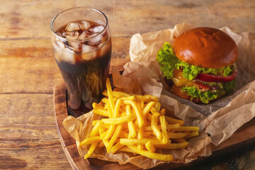 Board with tasty french fries, burger and glass of cola on wooden background, closeup
