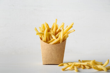 Paper bag with tasty french fries on light background