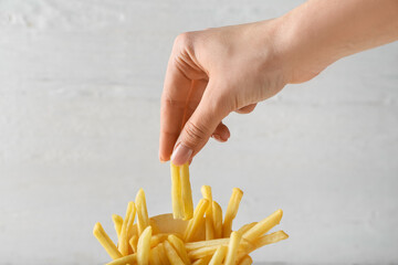Woman eating tasty french fries on light background, closeup