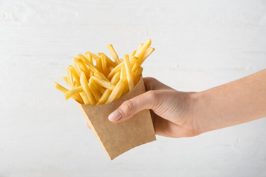 Female hand with tasty french fries in paper bag on light background