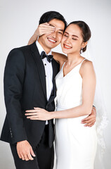 Young attractive Asian couple, bride and groom, woman wearing white wedding dress. Man wearing black tuxedo, teasing each other. Concept for pre wedding photography