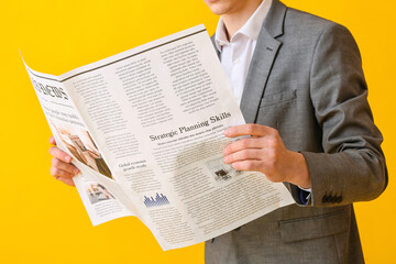 Young businessman reading newspaper on color background