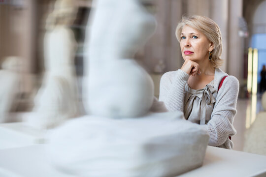 Adult glad female looking at artwork sculpture in the museum indoors
