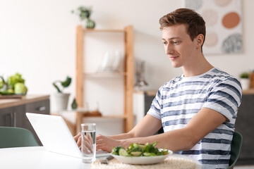 Young man using laptop while cooking in kitchen