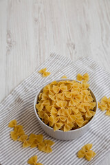Dry Organic Farfalle Pasta in a Bowl on a white wooden surface, side view. Copy space.