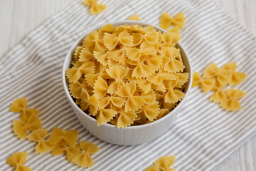 Dry Organic Farfalle Pasta in a Bowl on a white wooden surface, side view. Close-up.