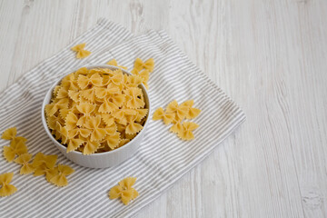 Dry Organic Farfalle Pasta in a Bowl on a white wooden surface, side view. Space for text.