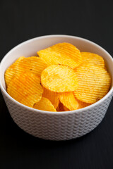 Ruffled Cheese Potato Chips in a Bowl on a black background, side view.