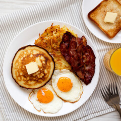 Full American Breakfast with Bacon, Hash Browns, Eggs and Pancakes on a plate on a white wooden table, top view. Flat lay, overhead, from above.
