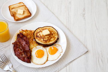 Full American Breakfast with Bacon, Hash Browns, Eggs and Pancakes on a plate on a white wooden background, side view. Space for text.