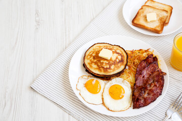 Full American Breakfast with Bacon, Hash Browns, Eggs and Pancakes on a plate on a white wooden background, side view. Copy space.