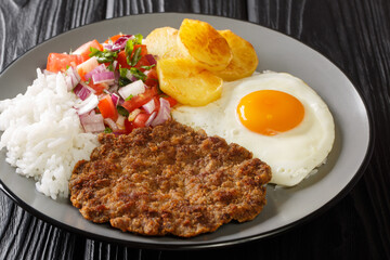 Authentic Silpancho Bolivian food from rice potatoes, beef, and fried eggs are topped with fresh salsa closeup in the plate on the table. Horizontal