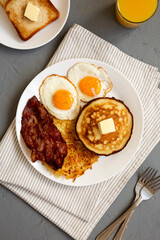 Full American Breakfast with Bacon, Hash Browns, Eggs and Pancakes on a plate on a gray background, top view.