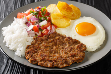 Silpancho Rice golden potatoes, beef, and fried eggs are topped with an onion and tomato salsa in this traditional Bolivian dish closeup in the plate on the table. Horizontal