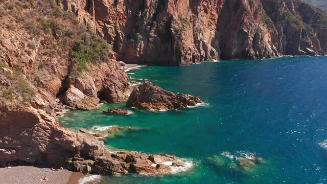 Aerial view of red rock cliffs mountain, sand beach, waves crushing on the beach. Colored sea, blue turquoise, high red cliffs on both side, green bushes of vegetation.