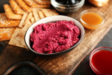 Composition with tasty beet hummus, snacks and sauces on dark background, closeup