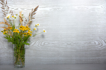 A bouquet of wildflowers in a glass vase on a wooden table with an empty place for text.
