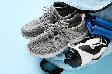 Backpack with sport shoes, bottle of water, skipping rope and earphones on color background, closeup
