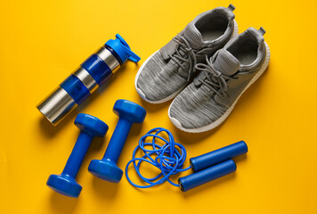 Obraz na płótnie Canvas Sport shoes, bottle of water, skipping rope and dumbbells on color background
