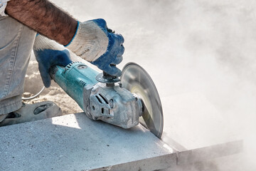 Hands of a pavement construction worker using an angle grinder for cutting the tiles