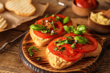 Fototapeta na wymiar Tasty bruschettas with tomato and hummus on wooden background, closeup