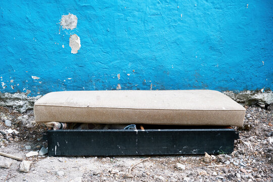 Old Dumped Junk Mattress And Bed In Front Of A Blue Wall