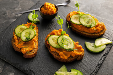 Tasty bruschettas with cucumber on dark background