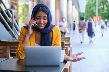 Young indian businesswoman speaking on the phone while working at a coffee shop.