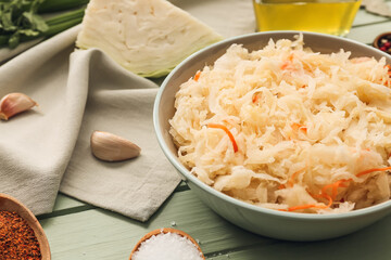 Bowl with tasty sauerkraut and ingredients on color wooden background
