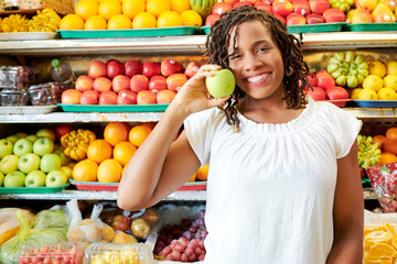 Portrait of African young customer smiling at camera while choosing the ripe fruits in the shop with shelves of fruits in the background