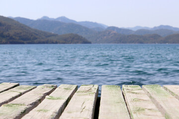 Beach vacation on the sea, background for summer holidays and travel. View from old wooden pier to deep blue water and misty mountains covered with forest