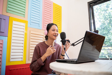 An asian vlogger is recording a podcast with a microphone and laptop computer