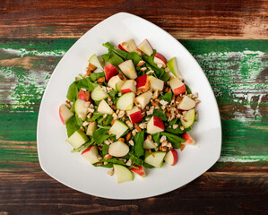 Healthy vegetarian rocket salad with dices apple, and chop almond in white dish place on colourful wooded table.  Concept for healthy