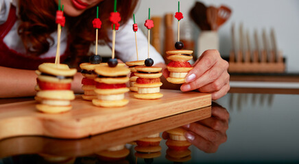 Closeup shot of delicious tasty yummy healthy small mixed fruit banana strawberry blueberry chocolate pancake appetizer decorated with stick on wooden cutting board made by pastry chef in background