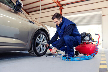 A car mechanic at the service station tries to inflate the tires on the car with the help of a...