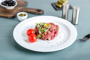 Plate with tasty beef tartare on color wooden background