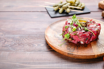 Plate with tasty beef tartare on wooden background, closeup