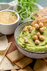 Bowl with tasty green pea hummus, chickpeas and crackers on table, closeup