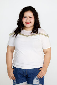 Portrait half body shot of Asian young happy cute friendly overweight fat teen long black hair female wears white shirt and short blue jeans stand smiling look at camera against white background.