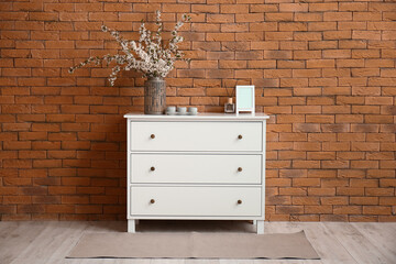 Vase with beautiful blossoming branches on chest of drawers in room