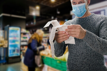 Male customer doing grocery shopping at supermarket and feeling confused by bill